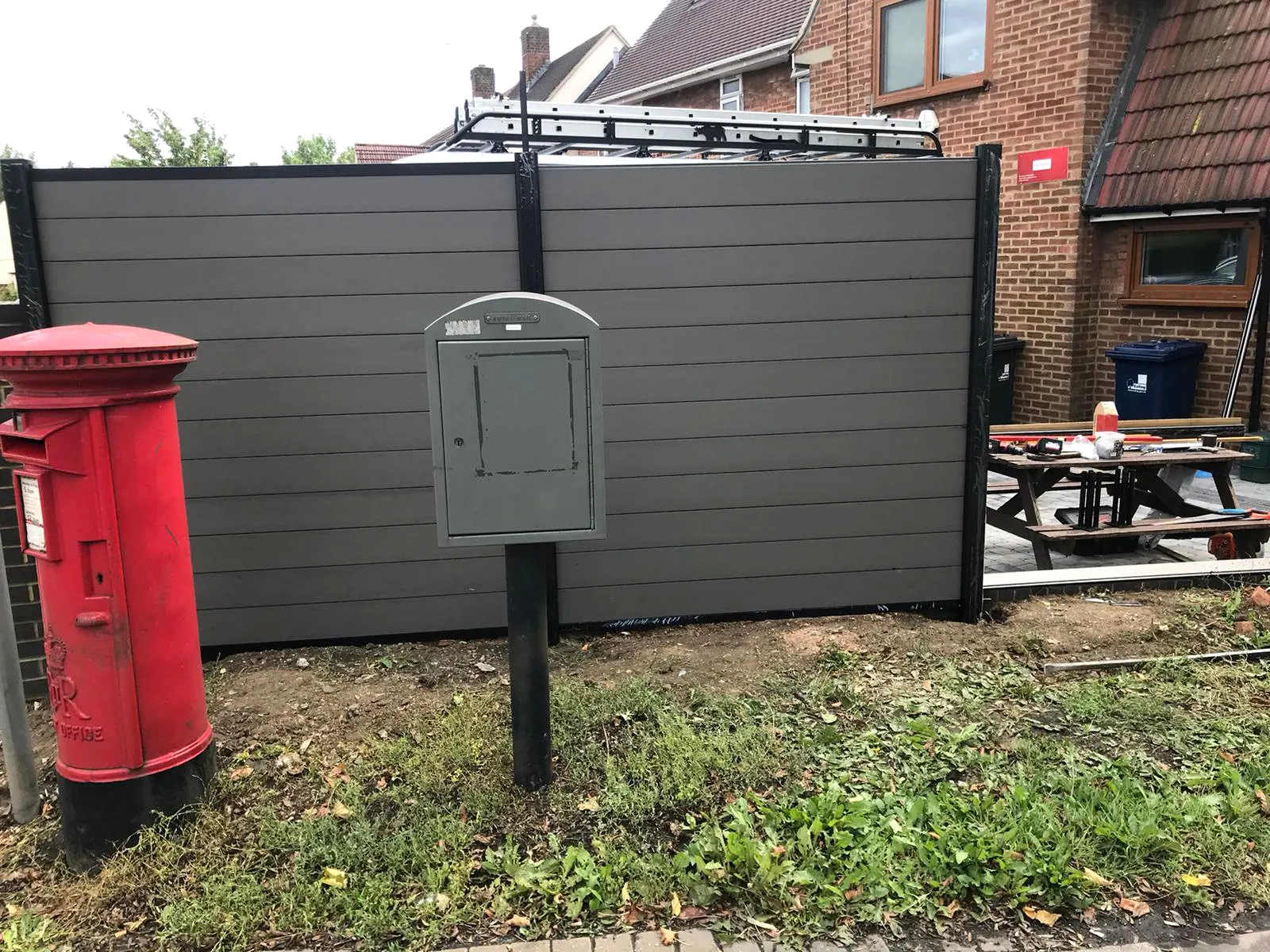 A grey composite fence beside a red Royal Mail pillar box
