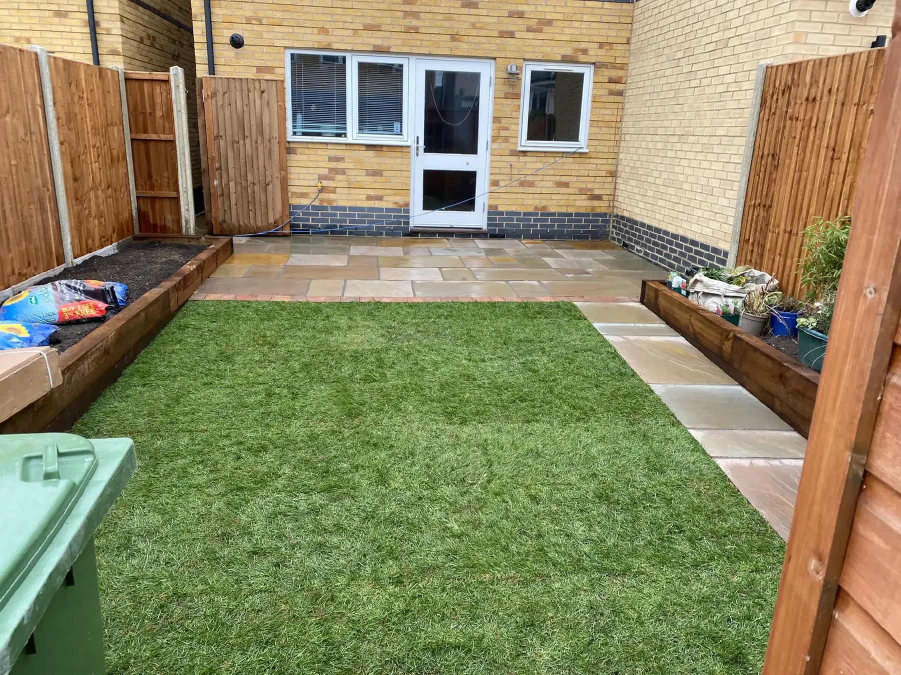 A new-build garden with fresh turf and sleeper beds