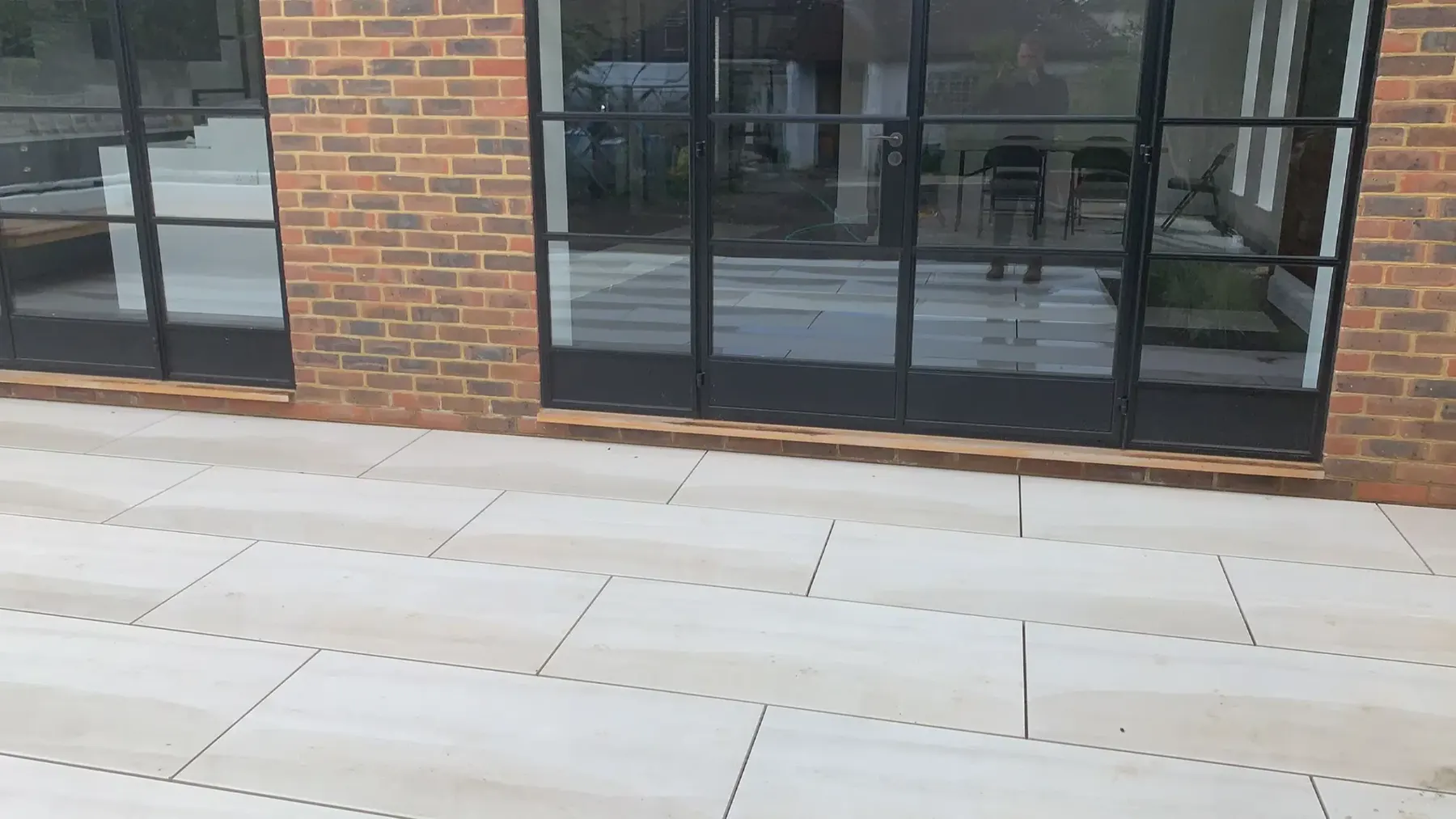 A pale porcelain patio laid level with Crittall-style doors on an extension